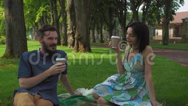 一个男孩和女孩在公园里举行了一次会议和野餐。 他们坐在草坪上说话喝咖啡。 微笑